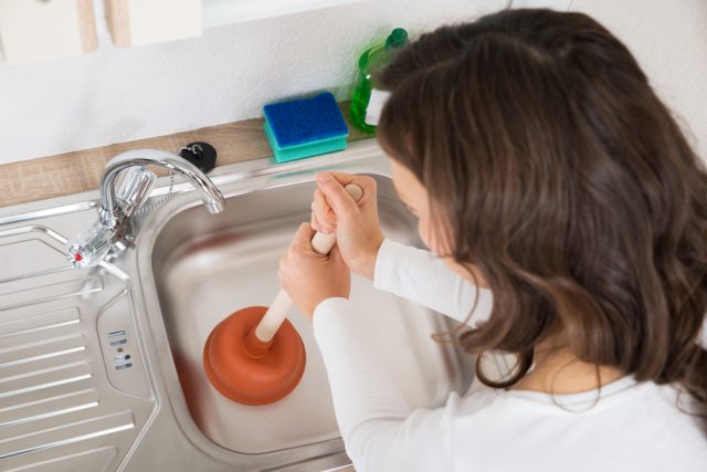 Woman Using Plunger In Sink - unblocking drains brisbane