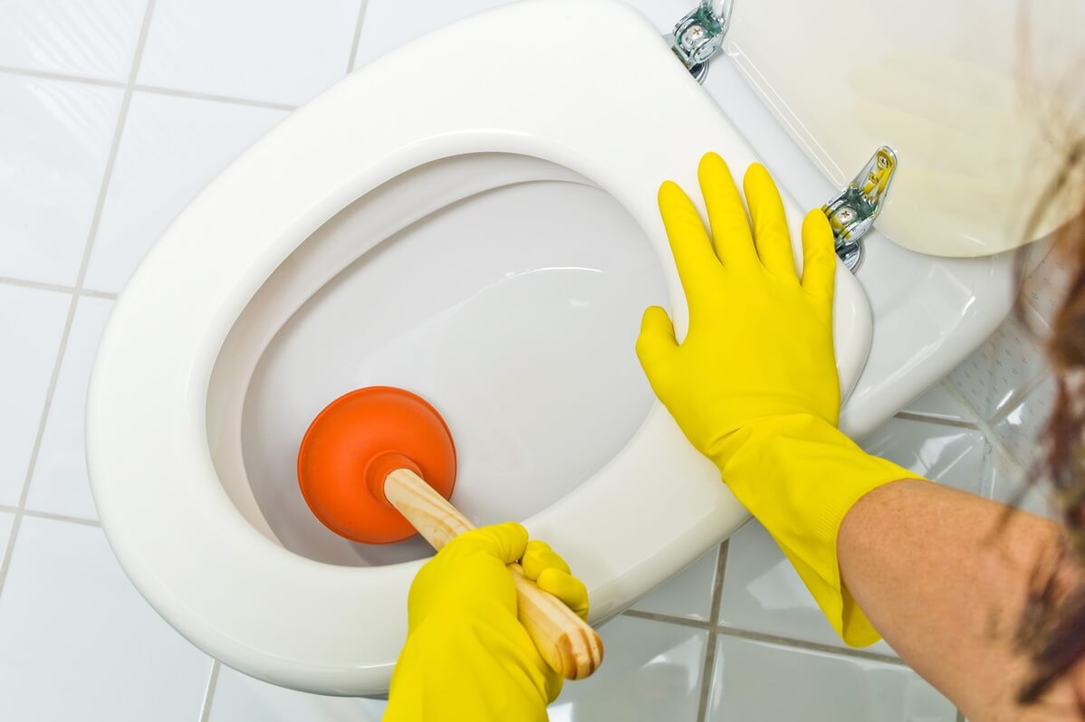 Gloved person unblocking a toilet with a plunger.