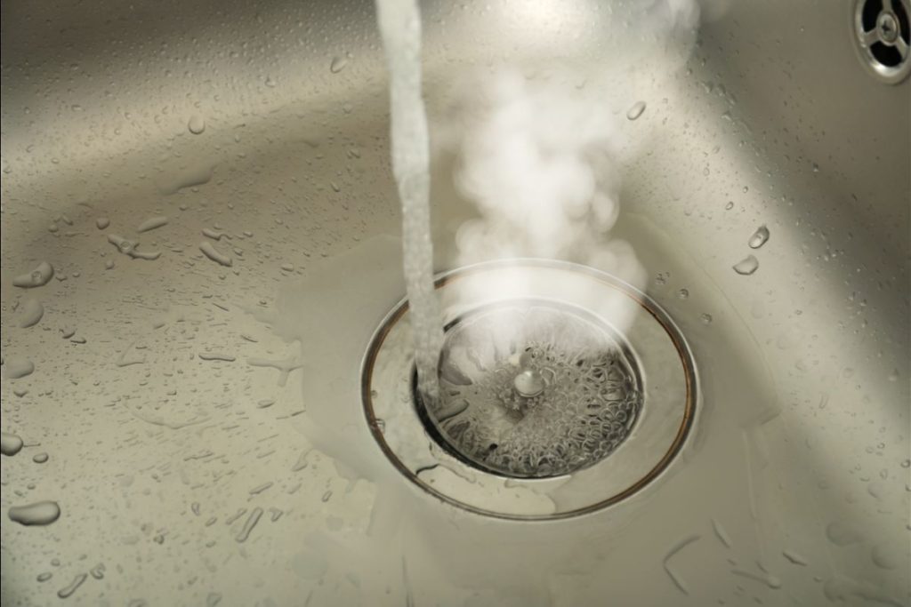 Pouring boiling water slowly down the drain to shift a blockage in the pipe.