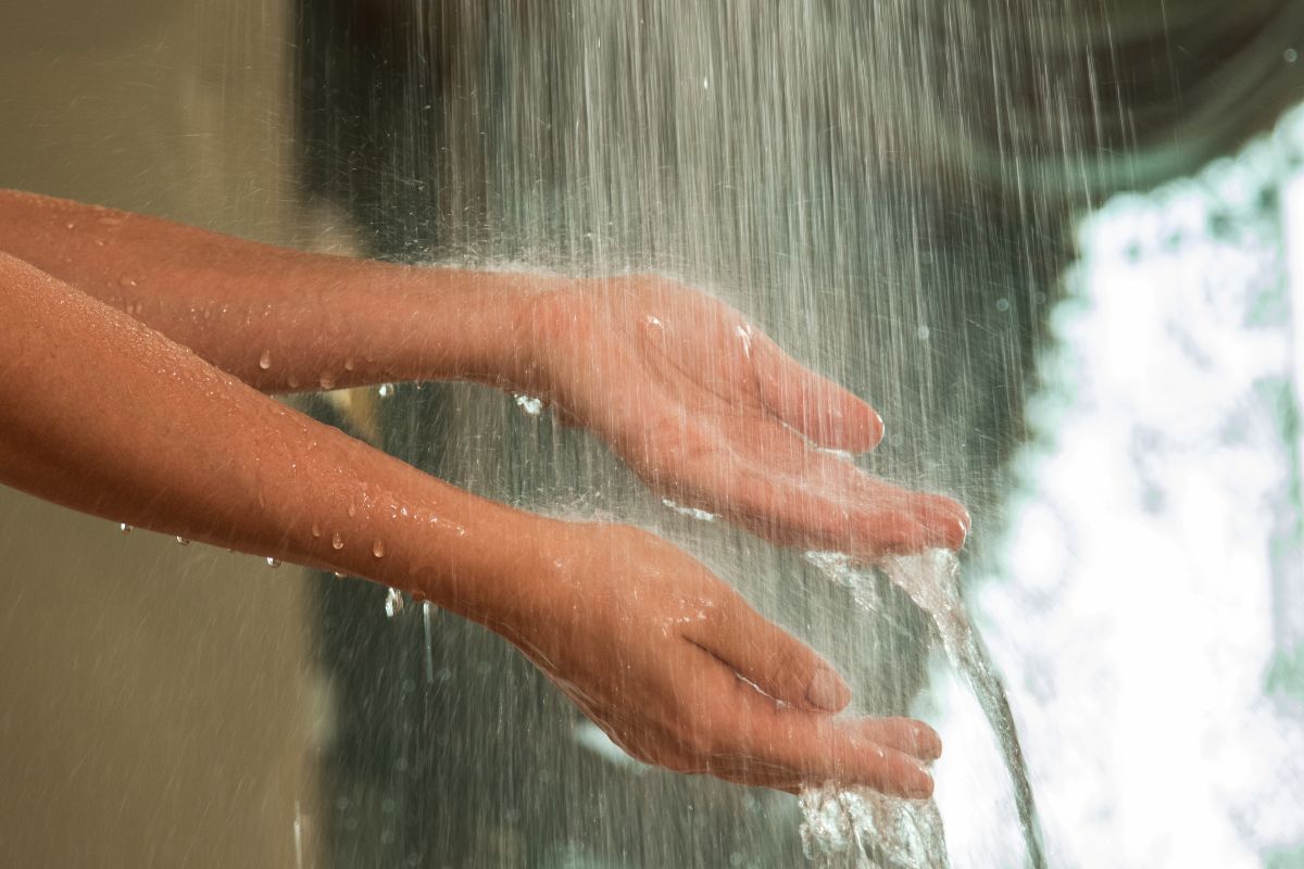 Woman with hands under hot water shower. Heat Pump systems are most cost effective.